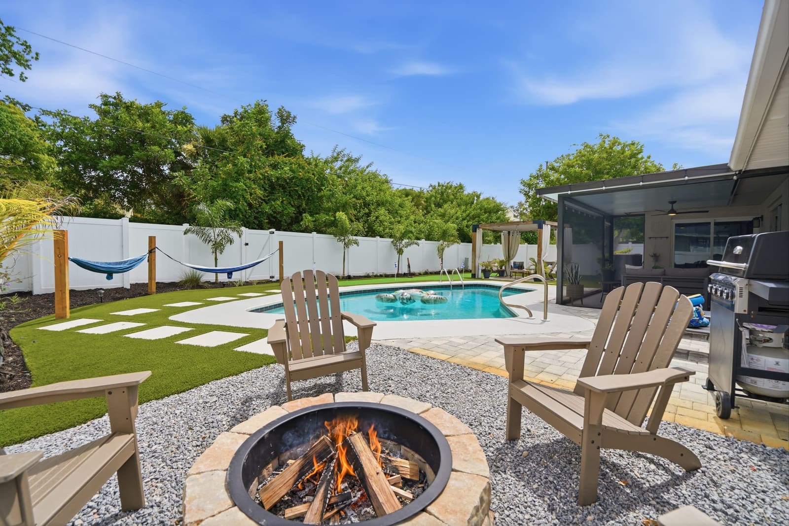 Adirondack chairs around a lit fire pit, the pool, hammocks and lanai behind.