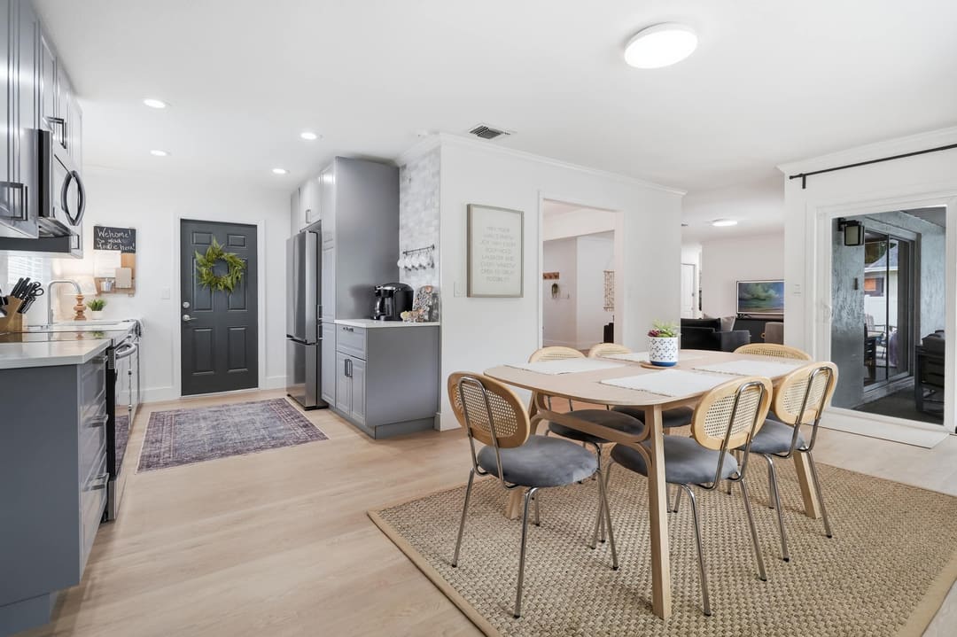 The table off the kitchen: a light wood table with cane chairs on a jute rug, under a flush ceiling light.