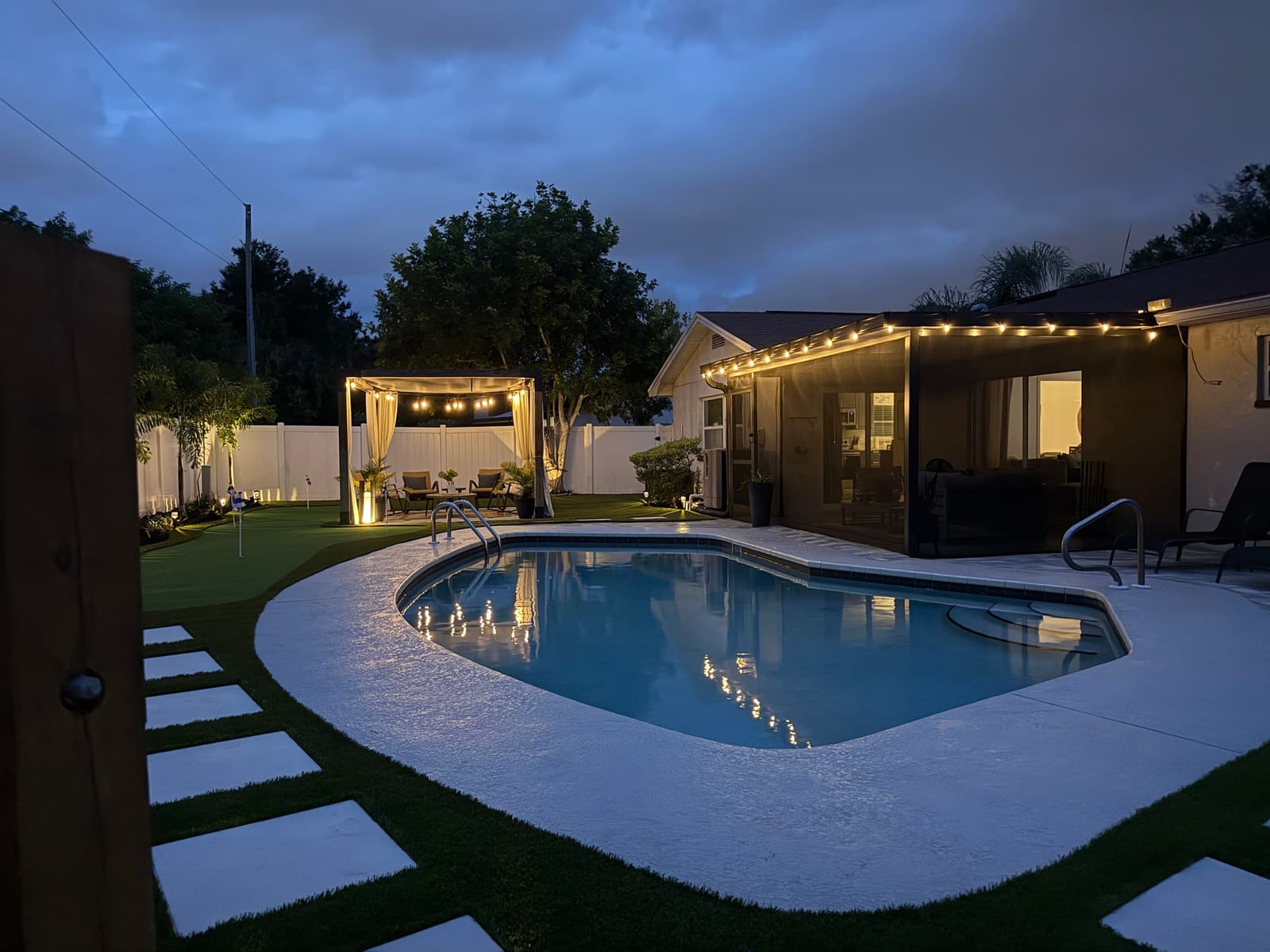 The lit cabana and the pool after sunset under heavy clouds.